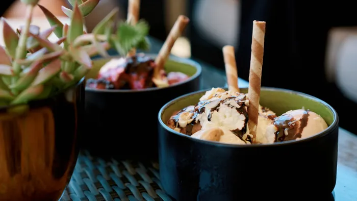 Schüssel mit Vanilleeis, Schlagsahne, Schokosirup und Waffelröllchen auf Glastisch
